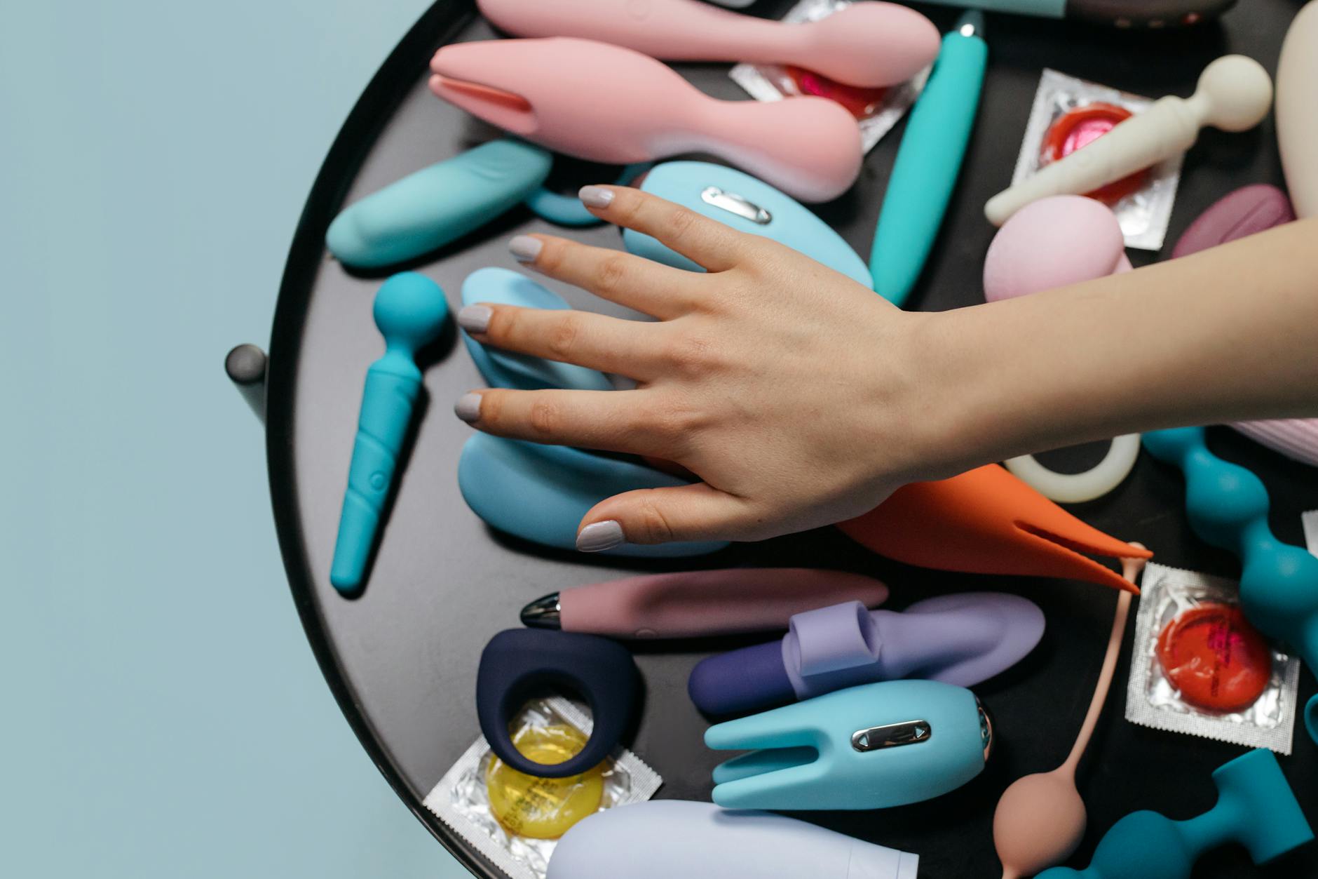 Vibrador azul rodeado de flores e fatias de laranja em fundo amarelo vibrante
