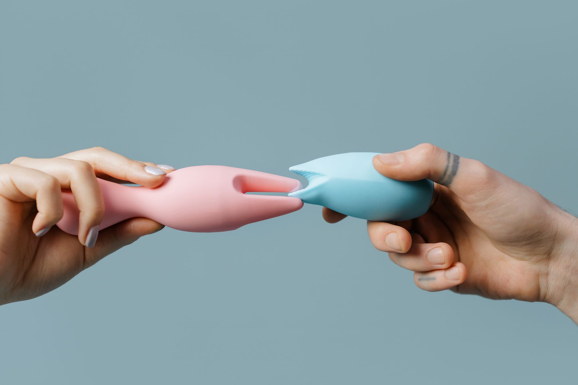 Mãos segurando brinquedos de silicone em cores pastel, representando exploração de prazer solo