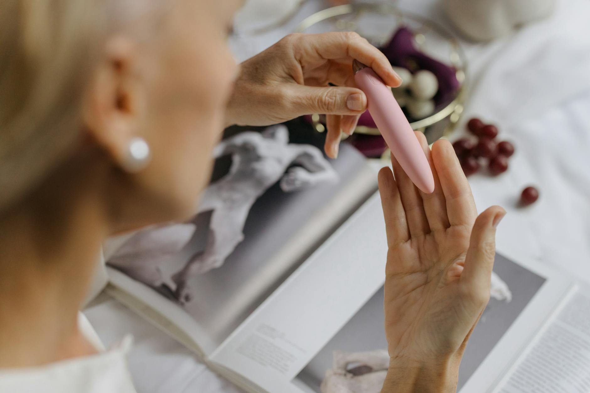 Mulher segurando um vibrador rosa com livros de arte ao fundo, enfatizando intimidade pessoal e redescoberta do prazer