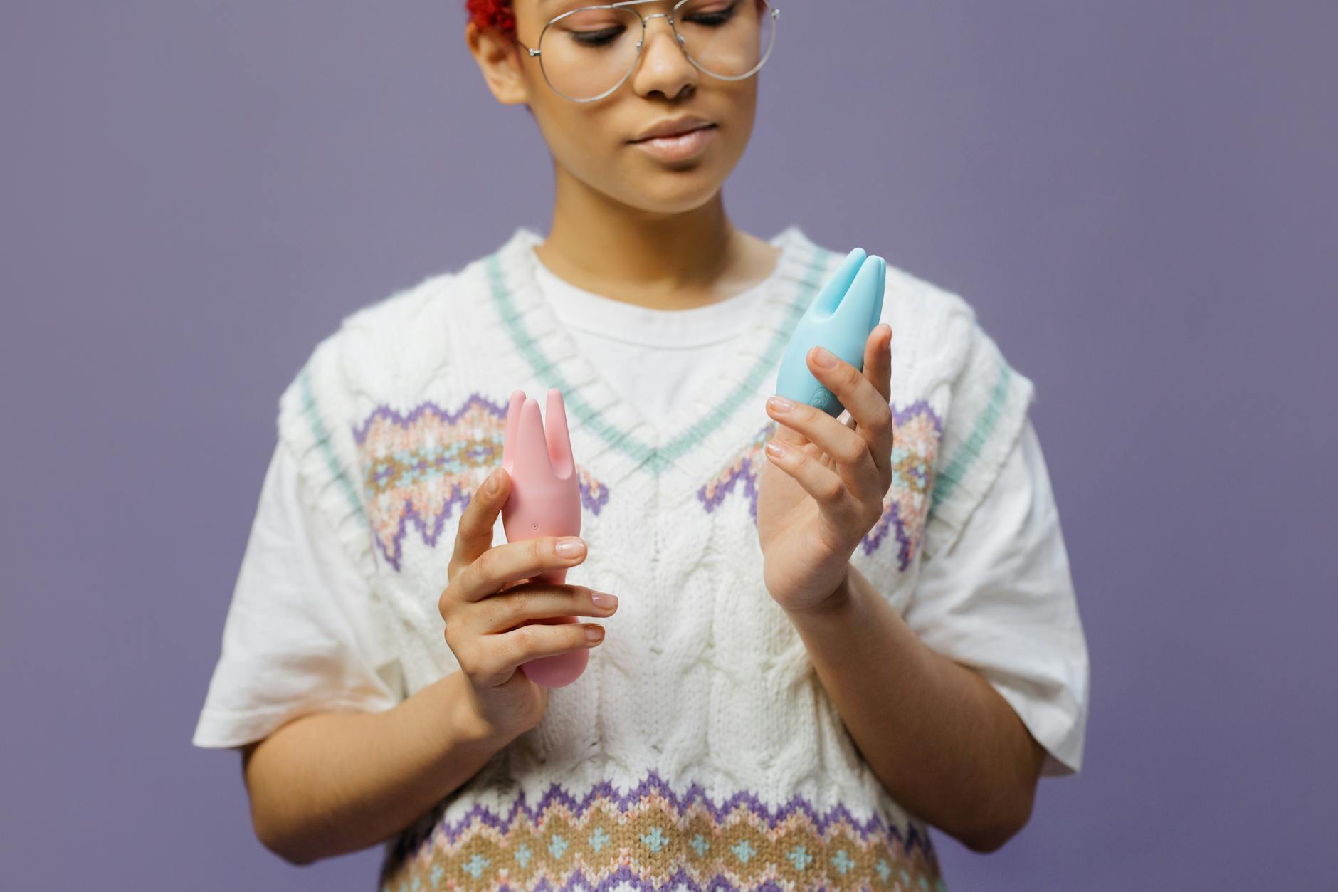 Mulher com óculos segurando vibradores de silicone rosa e azul de forma contemplativa.