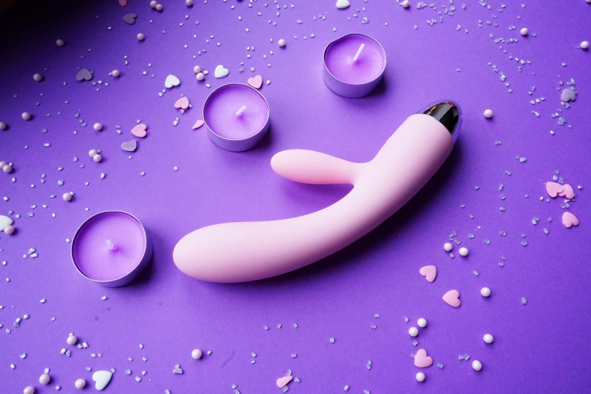 Mão segurando um vibrador laranja contra um fundo roxo minimalista, simbolizando sensualidade moderna e recuperação gradual